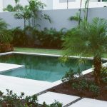 A pool surrounded by trees and plants in front of a white building