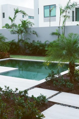 A pool surrounded by trees and plants in front of a white building